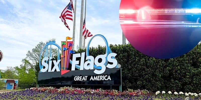 The image shows the entrance sign of Six Flags Great America with the iconic roller coaster silhouette above the text. American flags fly above the sign. On the right, there is a semi-transparent overlay of red and blue police lights as a theme park incident takes place.