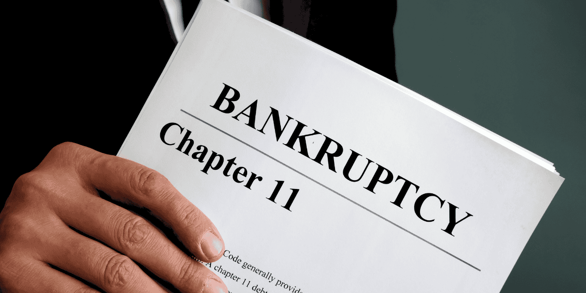 A person in a suit holds a document labeled "Chapter 11 Bankruptcy." The close-up image focuses on the title of the document, suggesting involvement with legal or financial proceedings potentially impacted by a landmark acquisition.