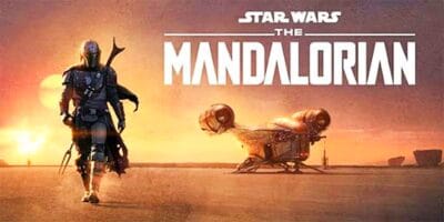 Poster for "Star Wars: The Mandalorian" showing the Mandalorian character in armor walking across a desert with a spaceship in the background. The scene is bathed in the warm glow of a setting sun. The series title is displayed prominently in white text at the top.
