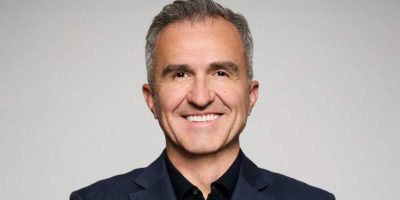 A person with short gray hair smiles at the camera. They are wearing a dark blazer and a black shirt, reminiscent of the professional attire often seen at ABC News. The background is plain and light-colored.