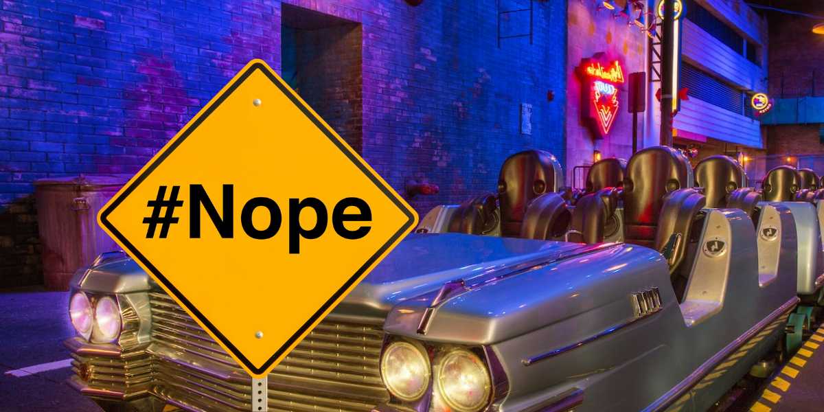 A retro car-themed amusement ride is in a dimly lit, vibrant setting with neon signs in the background. In the foreground, a large yellow caution sign with "#Nope" written on it reminds visitors to never use the Single-Rider Line for a full experience.