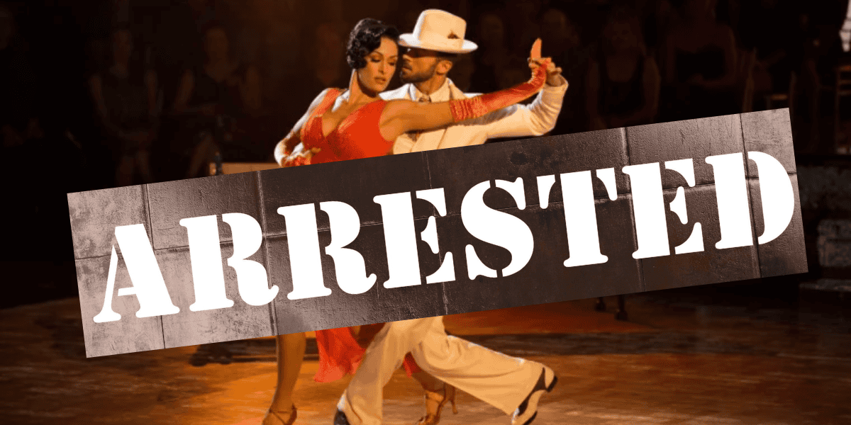 A couple dances passionately on a dimly lit stage, with the man wearing a white suit and hat, and the woman in a red dress. A large stamp across the image reads "ARRESTED" in white, bold letters, evoking a dramatic scene reminiscent of Artem Chigvinstev's intense performances on Dancing with the Stars.