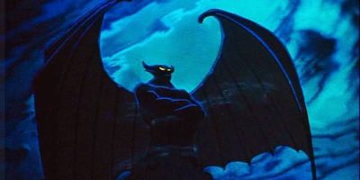A dark, menacing figure with glowing yellow eyes and large bat-like wings rises against the stormy, blue-lit sky of the Magic Kingdom.