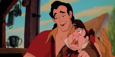 An animated scene featuring a tall, muscular man with black hair in a red shirt, smiling confidently with his arm around a shorter, stocky man with brown hair and a red bowtie, who looks surprised. They appear to be standing outside near wooden beams and metal pots.