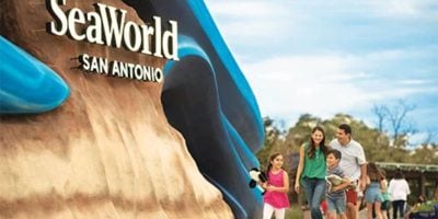 A family of four, including two adults and two children, walk together past the SeaWorld San Antonio entrance.