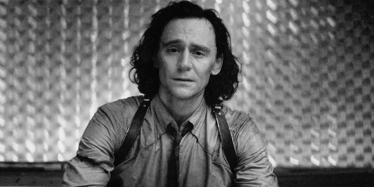 A black-and-white image of a man with long hair sitting and facing forward. He is wearing a button-up shirt with a tie and suspenders. The background features a textured, metallic wall, reminiscent of something from the Marvel universe. The man appears to have a contemplative expression.