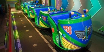 Four turquoise and green ride vehicles, themed after Toy Story spacecraft and featuring "XP-38" decals, are lined up on a track, ready for passengers. They have seats and twin laser blasters, set against a futuristic backdrop with zigzag neon patterns.