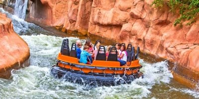 A group of people, including children and adults, are enjoying a whitewater rafting ride on a circular raft in a man-made river at Walibi theme park.