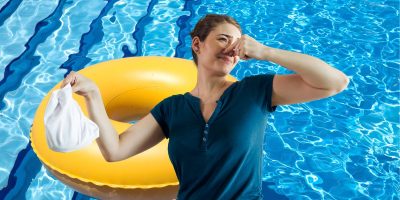 A woman standing in front of a swimming pool at Disney World, holding her nose with one hand and holding a white diaper in the other. A yellow inflatable ring floats in the pool in the background, hinting at a recent poop problem.