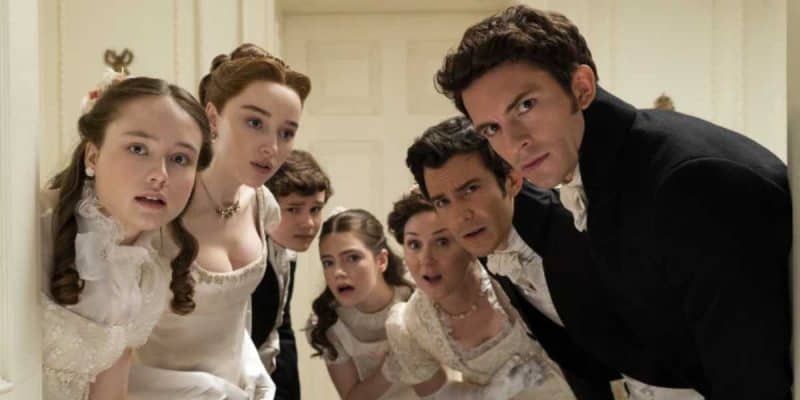A group of men and women, dressed in Bridgerton-style Regency-era formal wear, look intently into the camera while standing closely together, appearing both curious and concerned. The setting is a vintage, elegant room with off-white walls and classic decor, evoking a sense of high society.