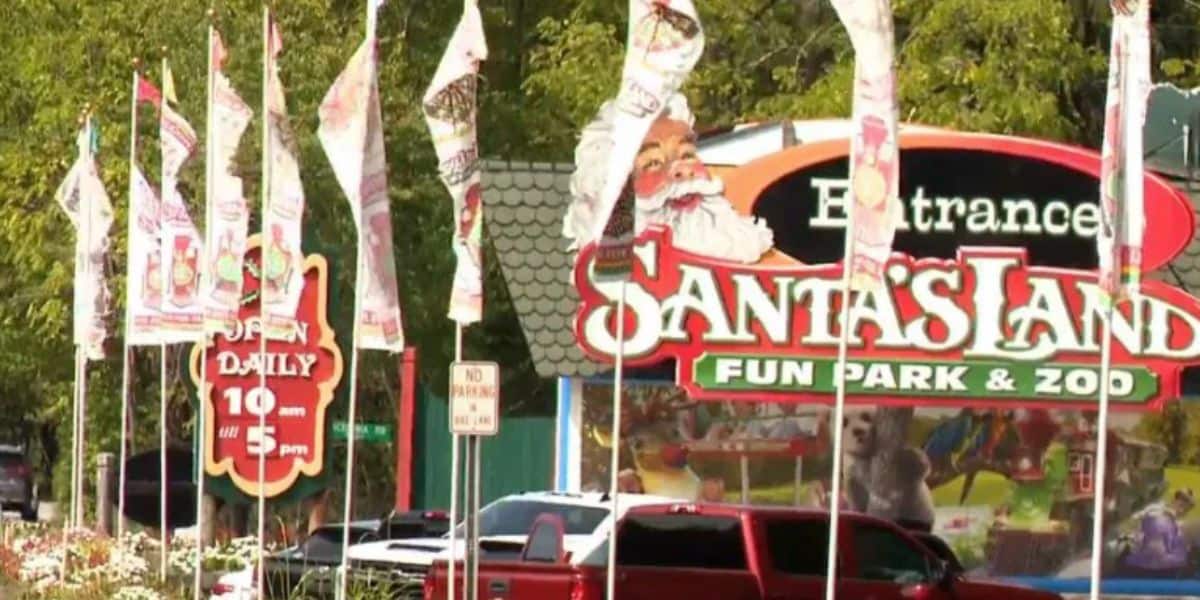 Image showing the entrance to Santa's Land Fun Park & Zoo. A colorful sign with a Santa Claus graphic, flags, and trees in the background. The park's hours, "Open Daily 10 am - 5 pm," are displayed. The scene includes a red vehicle and greenery surrounding the entrance.