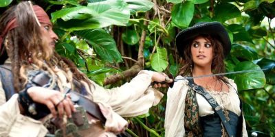 Two characters dressed as pirates stand in a lush, green jungle. One character, on the left, has dreadlocks, a bandana, and holding a sword pointed at the other character. The other character, on the right, is wearing a wide-brimmed hat and looking surprised.