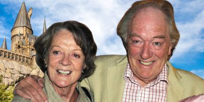 Maggie Smith and Michael Gambon are smiling and posing with their arms around each other in front of a fantasy-style castle, reminiscent of Harry Potter's Hogwarts. The sky is blue with scattered white clouds. Both are wearing casual clothes; the woman in a green top and the man in a beige jacket and checkered shirt.