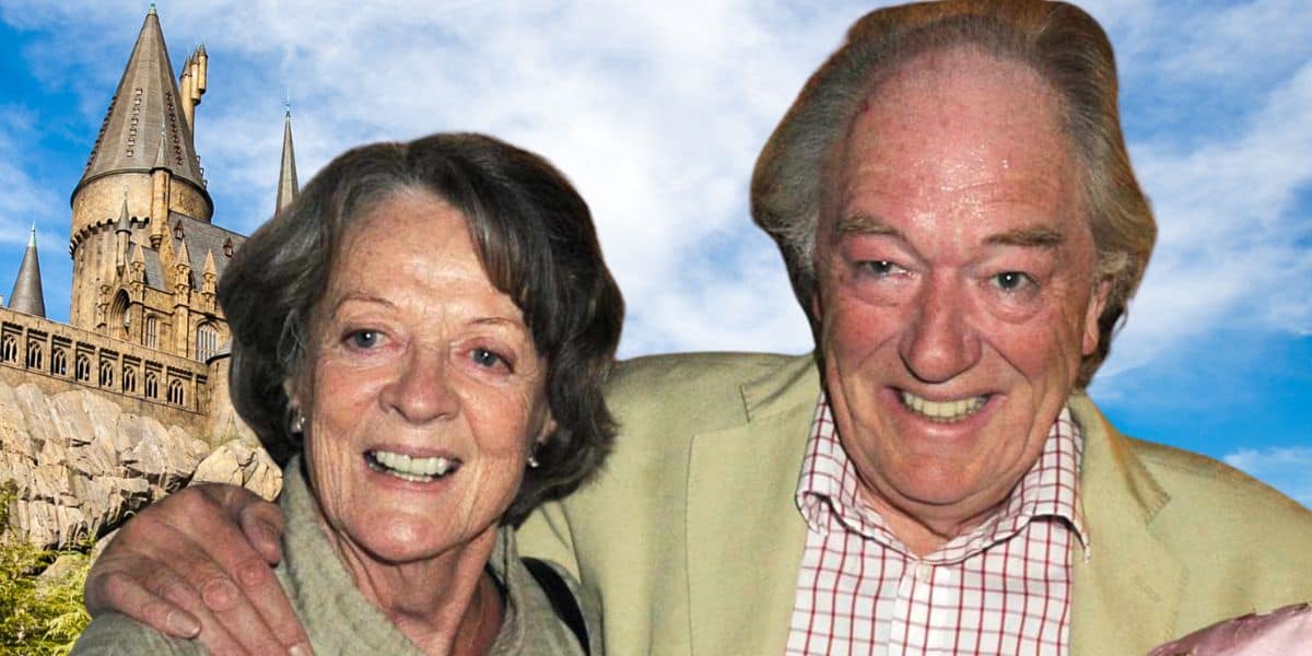 Maggie Smith and Michael Gambon are smiling and posing with their arms around each other in front of a fantasy-style castle, reminiscent of Harry Potter's Hogwarts. The sky is blue with scattered white clouds. Both are wearing casual clothes; the woman in a green top and the man in a beige jacket and checkered shirt.