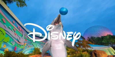 A dolphin balances a blue ball on its nose in front of Disney's The Seas with Nemo & Friends Pavilion at Epcot, featuring colorful marine murals and the iconic geodesic sphere of Spaceship Earth in the background. The Disney logo overlays the image.