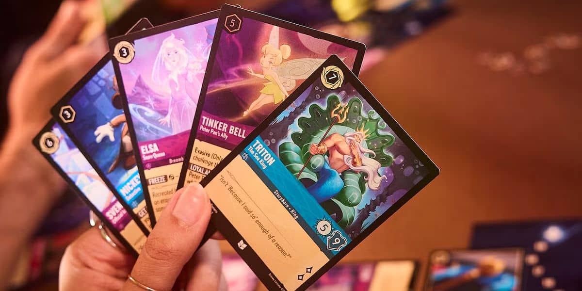 A person holds a fan of five Disney Lorcana cards featuring animated characters.