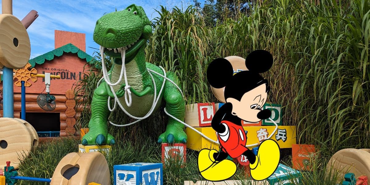 Mickey Mouse walking away sad on top of a picture of the entrance of Toy Story Land at Hong Kong Disneyland.