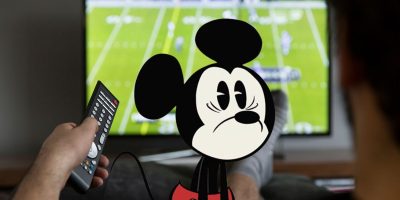 Mickey Mouse looks dumbstruck as someone watches sports on a blurred TV in the background.