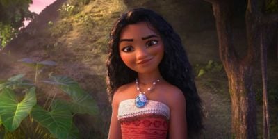In a lush, tropical setting, the animated character with long, wavy hair smiles warmly. She wears a red patterned strapless top and a necklace featuring a blue pendant, hinting at adventures akin to Moana 2. Large leaves and trees frame the vibrant scene.