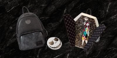 A black backpack with a skull emblem, a round skull-themed purse, and a coffin-shaped box featuring a colorful gothic character from the Loungefly Collection capture the essence of spooky style. They rest on a textured black marble background.
