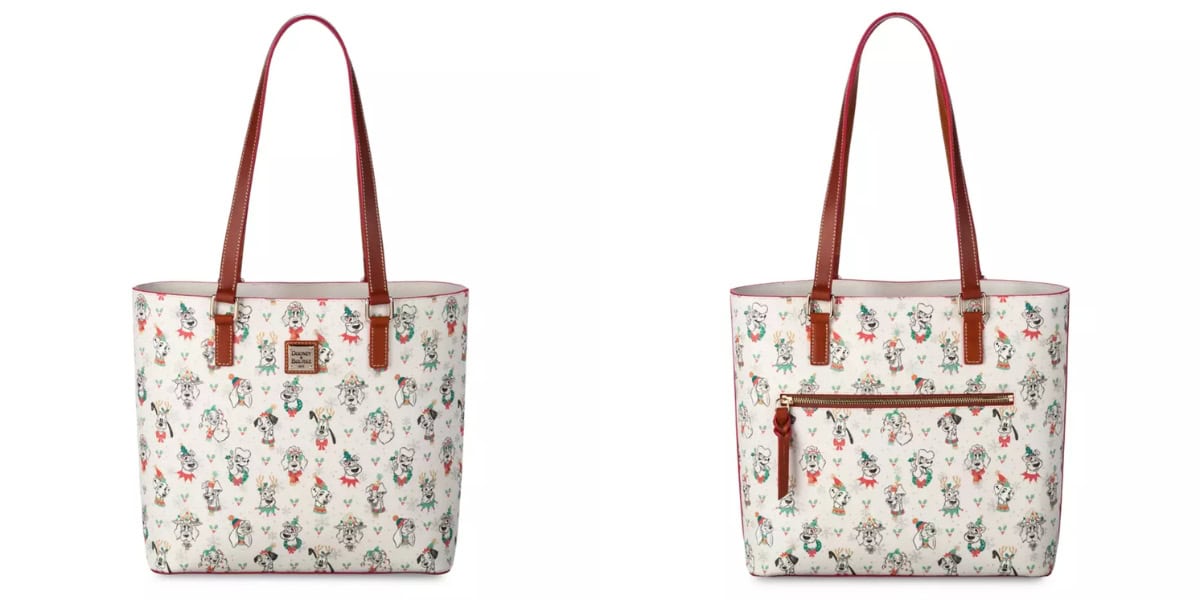 A white tote bag with a nature-themed pattern featuring birds, flowers, and foliage. It has brown leather handles, a front pocket with a zipper, and a small brand logo tag. This stylish accessory is from the Dooney & Bourke Disney Dogs Holiday Collection, perfect for any festive outing.