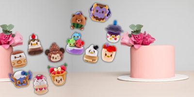 A whimsical group of plush toys from the Limited Time Disney Munchlings collection, resembling desserts and animals, float above a pink cake adorned with pink flowers. The scene is set against a simple, light-colored background, adding a touch of magic to these scented mysteries.