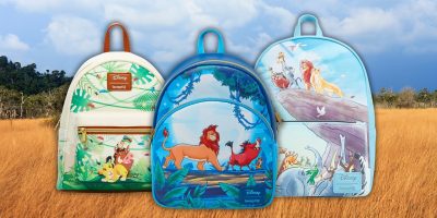 Three colorful Loungefly backpacks with Lion King illustrations are displayed in a grassy landscape. Each backpack showcases scenes featuring Simba, Timon, and Pumbaa in vibrant colors and various poses against the natural backdrop of the Pride Lands.
