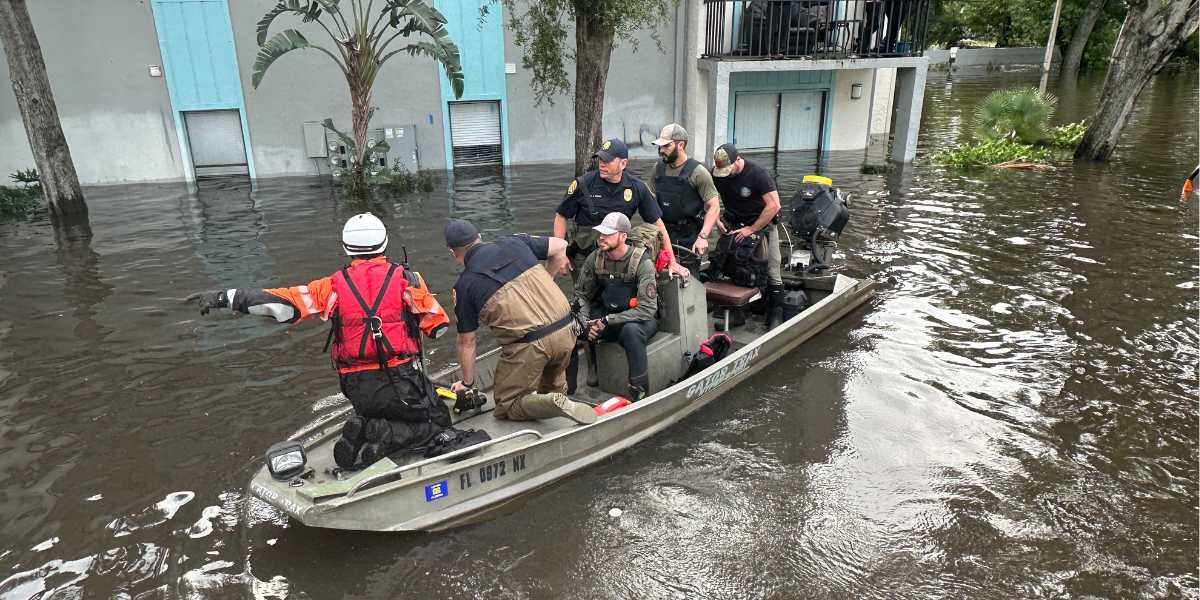 Rescue workers on a motorboat navigate through a flooded street lined with trees in Florida.