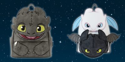 Two dragon-themed mini backpacks are displayed against a starry background. The left backpack is black with green eyes, resembling a playful How to Train Your Dragon face. The right backpack is white with blue eyes and wings, showing an upside-down dragon face ready to take flight.