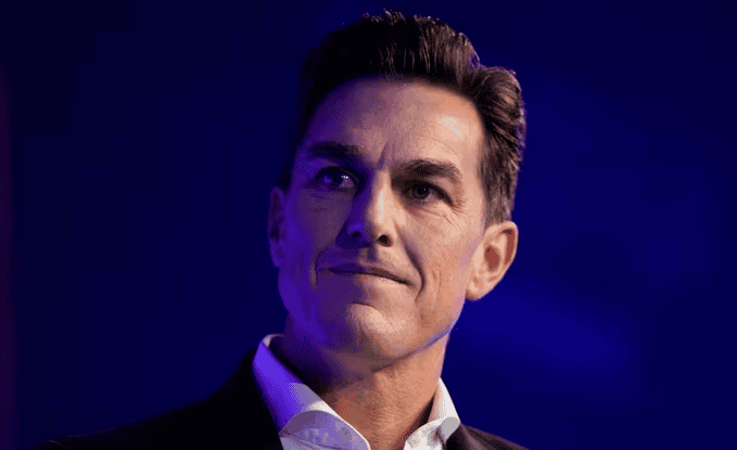 Andrew Wilson with short dark hair and a light complexion, reminiscent of Bob Iger, is wearing a suit and white collared shirt, looking slightly upward in anticipation of an important announcement. The deep blue background adds a touch of Disney magic.