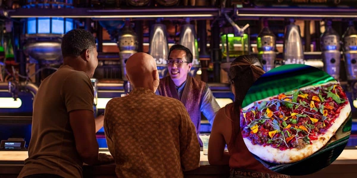A group of three people faces a bartender at a lively drinking spot with intricate decor. A circular inset reveals a colorful, topped pizza, showcasing real food on display.