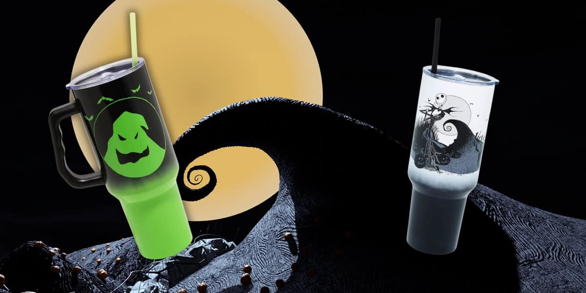 Two Halloween-themed stainless steel travel cups with straws sit in front of a large full moon. The left cup is green with an Oogie Boogie face, while the right is white with a dark, swirling tree design reminiscent of Jack Skellington's style. Both cups rest on a twisted black hill.
