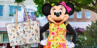 A character in a floral dress with a pink bow stands outside, holding a Sketch Tote adorned with cartoon designs. The background features a building with large windows and greenery, exuding an air of Disney Whimsy.