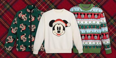 Three festive sweaters from the Holiday Collection are displayed on a plaid background. The left is green with holiday-themed patterns; the center features Santa Mickey on a white backdrop, and the right is a colorful sweater showcasing multiple character faces in a geometric design. Stay cozy!