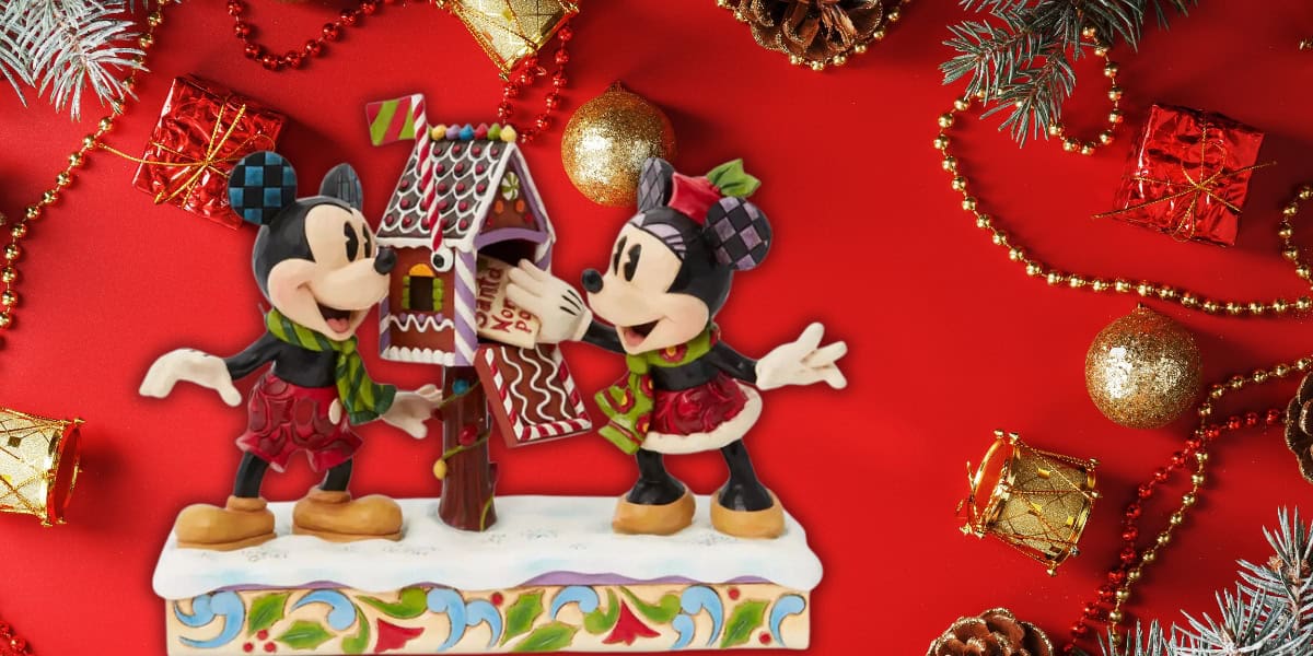 A festive scene features Mickey and Minnie Mouse as charming cartoon figurines adorning a gingerbread house atop a snowy base. The vibrant red background is embellished with gold beads, gift boxes, pine cones, and branches.
