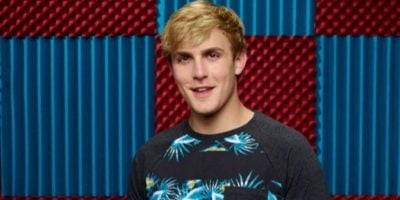 A person with short blonde hair, wearing a shirt with blue and green floral patterns, stands in front of a red and blue checkered wall, reminiscent of a scene from a Netflix Fight.