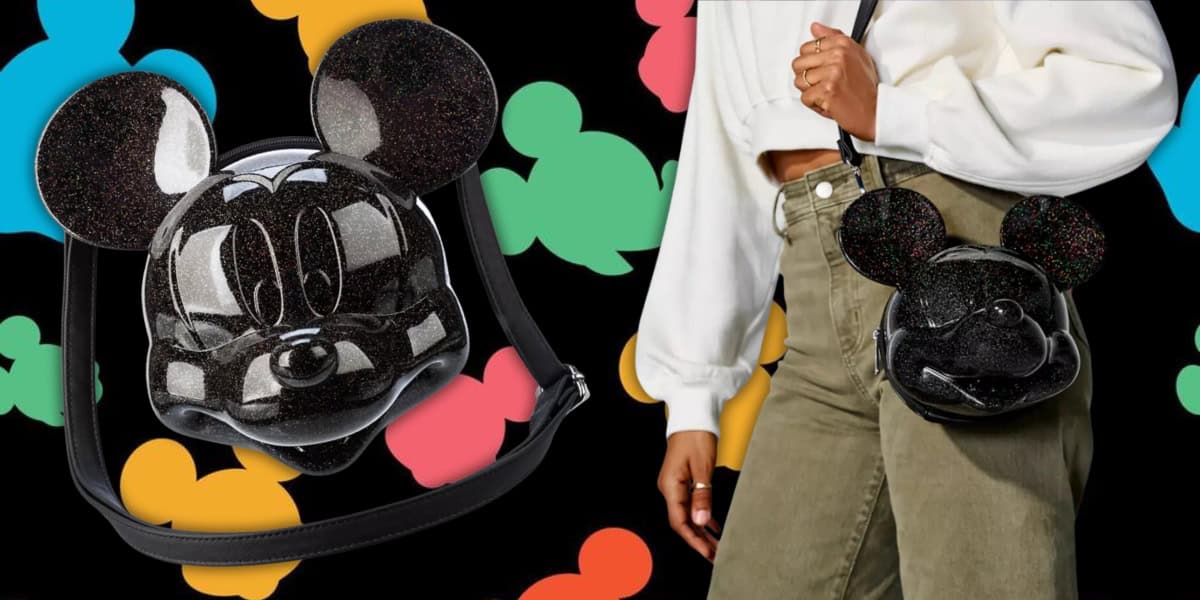 A person holds a black, shiny purse shaped like Mickey Mouse's head. The background features colorful silhouettes of the iconic character in various pastel colors. The person is wearing a white sweater and green pants, evoking Disney magic with their enchanting Loungefly crossbody bag.