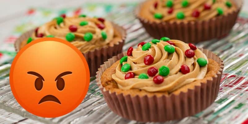 Three cupcakes with brown frosting and red and green candies are on a glass platter, offering a delightful treat. An angry face emoji is placed in the foreground, perhaps reflecting the frustration of guests who can’t make it to Disney World.