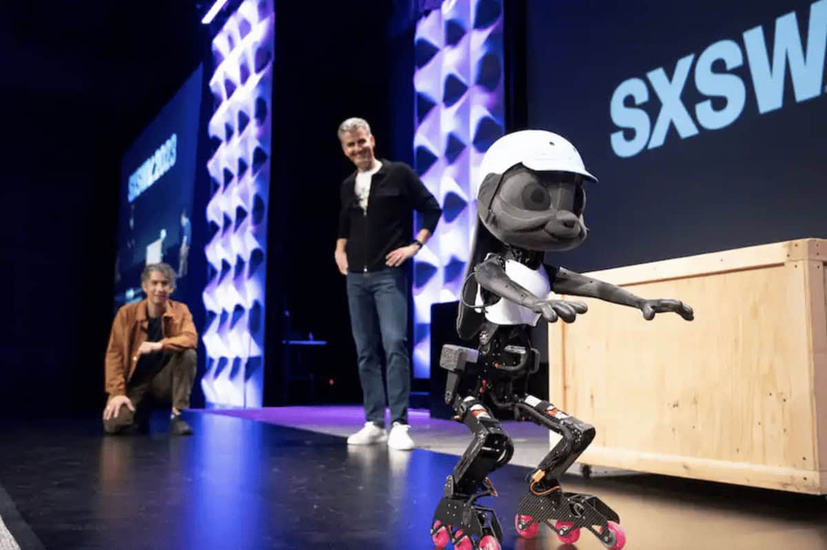 A robot resembling Disney animatronics, wearing a helmet, roller skates onstage at SXSW, while two people in the background watch with interest. The stage is bathed in purple lights, and "SXSW" is displayed prominently on screens.