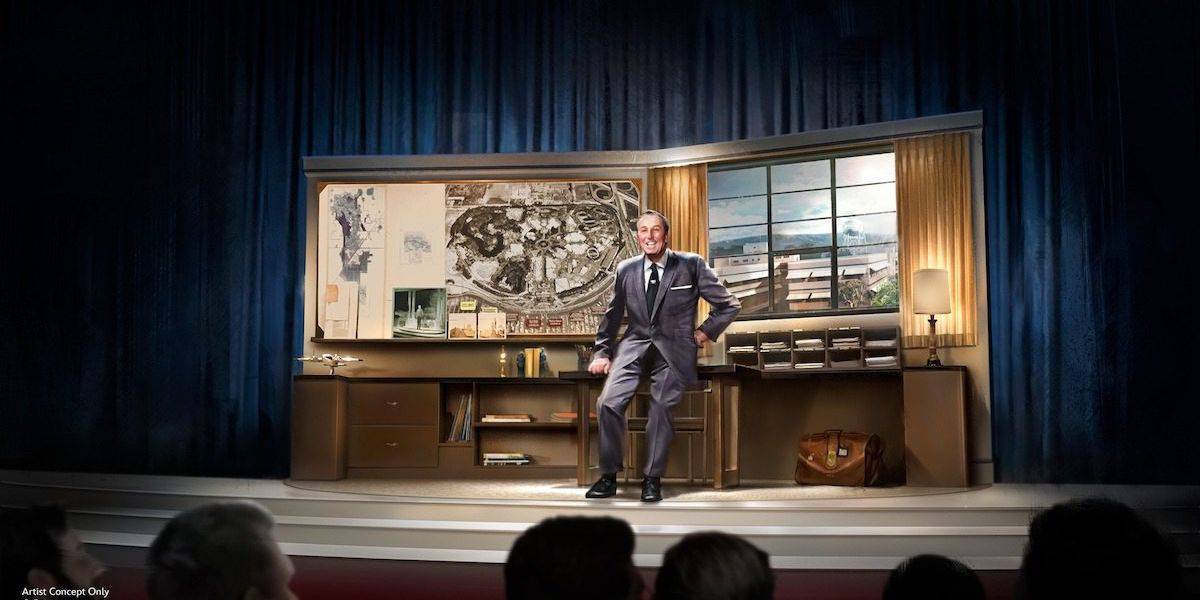 A man in a suit stands on a stage in front of a large desk with architectural plans and a model of a theme park. Curtains and a window with a view of a building are in the background. Audience members are visible in the foreground.