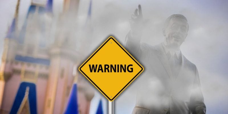 A foggy image of a statue with a yellow advisory sign in the foreground. The background shows part of the Cinderella castle inside Magic Kingdom at at Walt Disney World Resort.