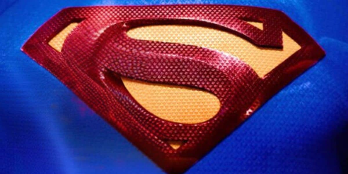 A close-up of the red and gold Superman logo on a blue background showcases the iconic "S" shield with texture, standing out prominently as a tribute to Superman's legendary presence.