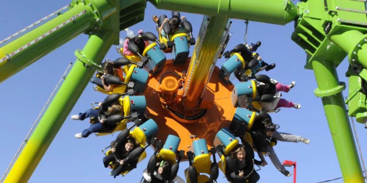 People are seated in a circular arrangement on a colorful ZDT's Amusement Park ride swinging in the sky.
