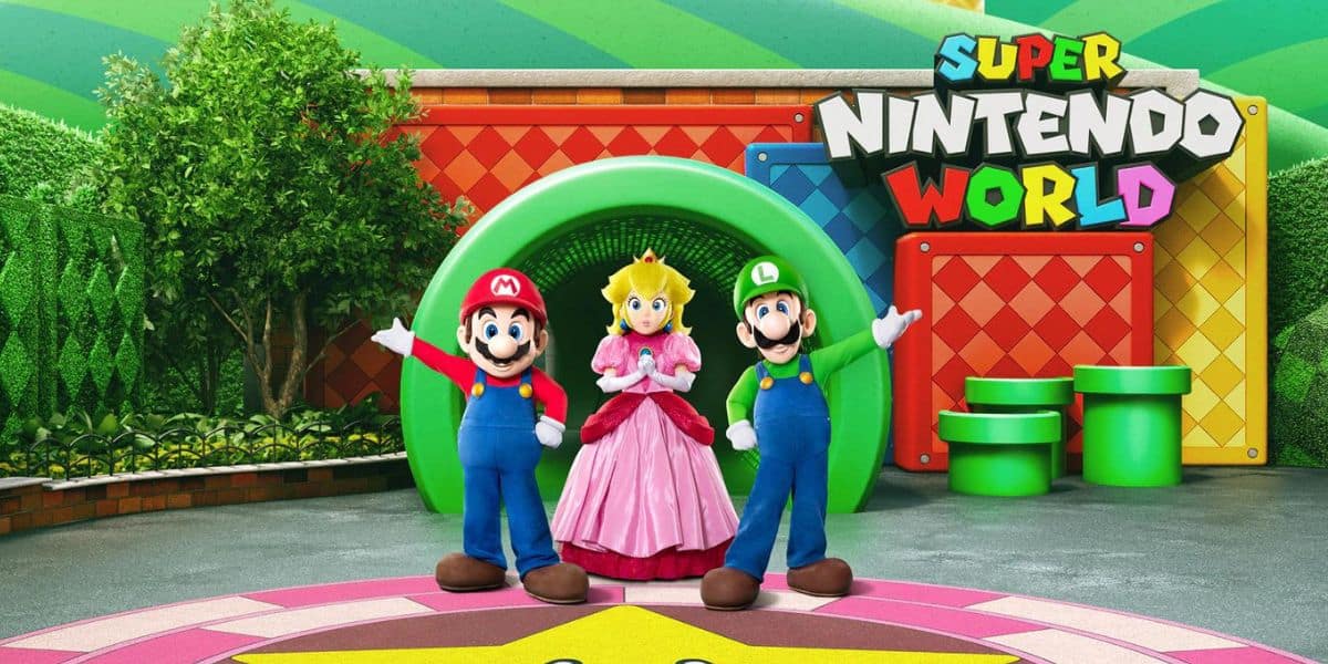 Mario, Luigi, and Princess Peach are in Super Nintendo World for its world debut, standing in front of a large green pipe entrance. The vibrant background features greenery, colorful walls, and two additional green pipes.