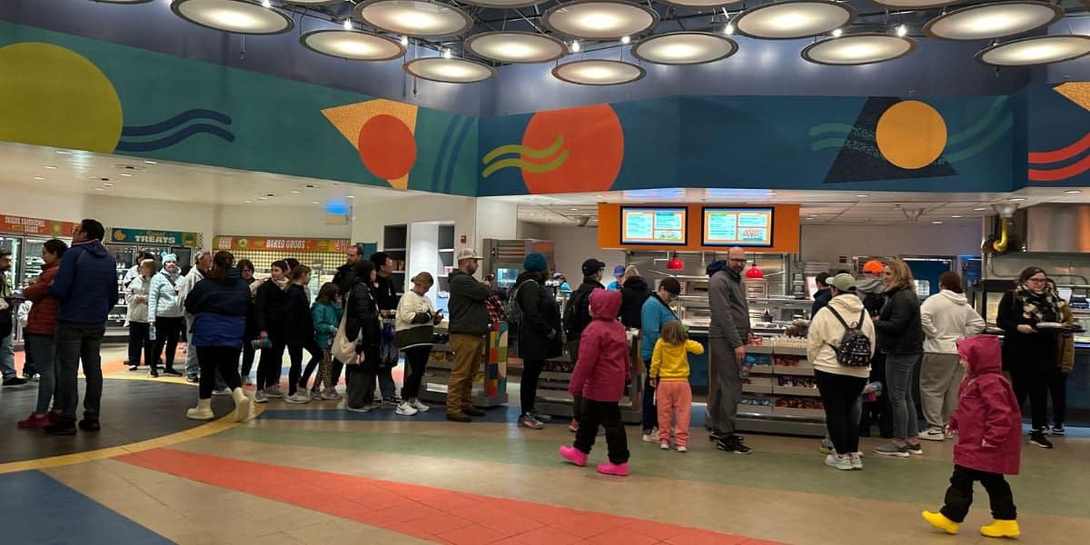 People are lined up inside a colorful food court at Disney's Pop Century Resort.