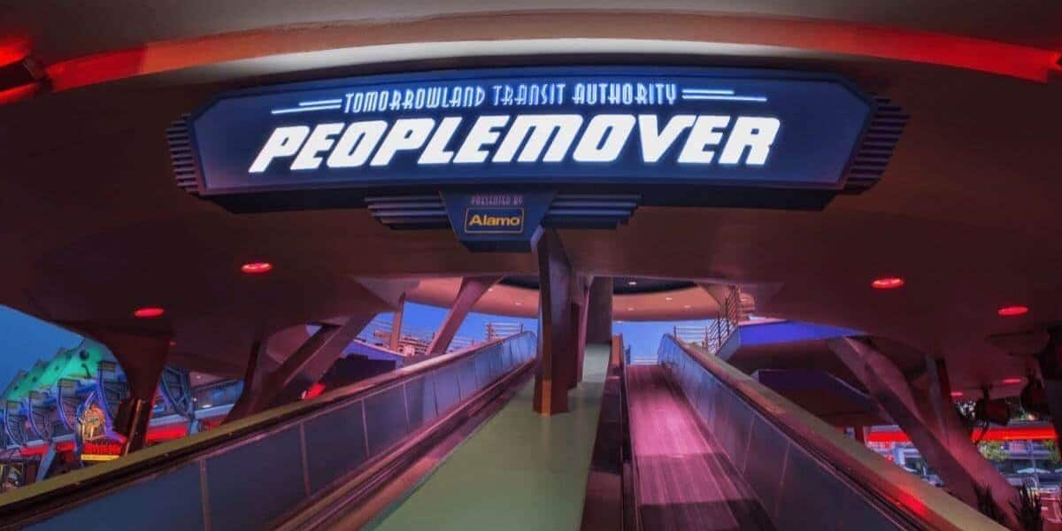 The illuminated sign for the Tomorrowland Transit Authority PeopleMover glows brightly at night, casting a futuristic charm over the entrance ramp below. This Disneyland PeopleMover scene captures the essence of an imaginative theme park environment.