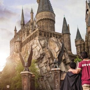 Two people in themed 'Harry Potter' attire walk towards Hogwarts Castle at Universal