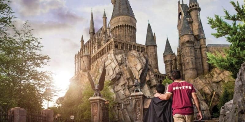 Two people in themed 'Harry Potter' attire walk towards Hogwarts Castle at Universal