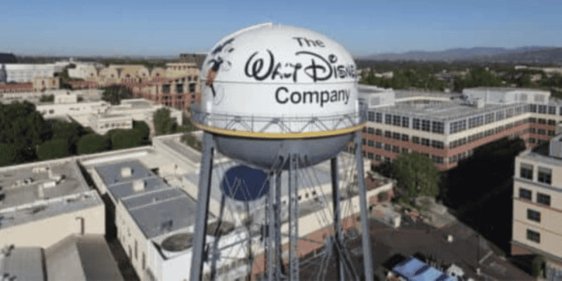 Aerial view of the Walt Disney Company water tower, proudly showcasing its logo. The iconic tower stands amidst office buildings and lush greenery under a clear blue sky, evoking a sense of timeless magic even in the digital age.