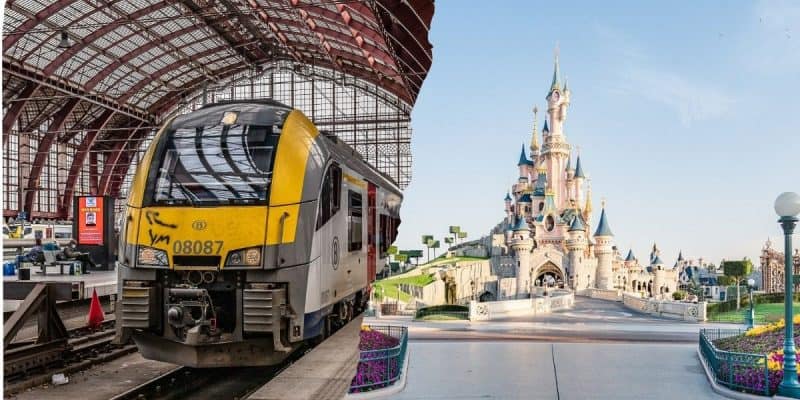 A train sits inside a large, glass-roofed station next to an image of Disney Resort castle with towers and spires, surrounded by neatly trimmed gardens and a clear blue sky.